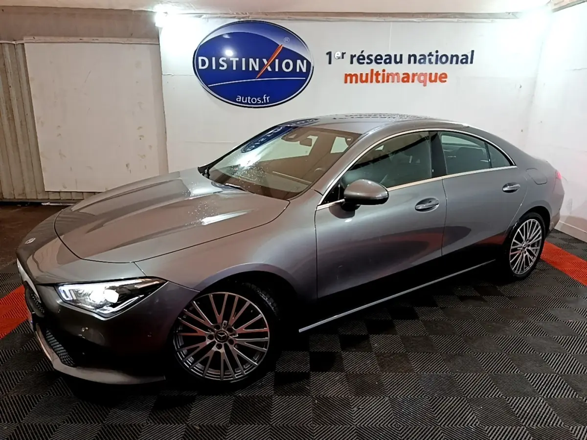 Vue 3/4 avant droit d'une Mercedes CLA 180 d Business Line gris clair avec jantes alliage et phares allumés en intérieur.