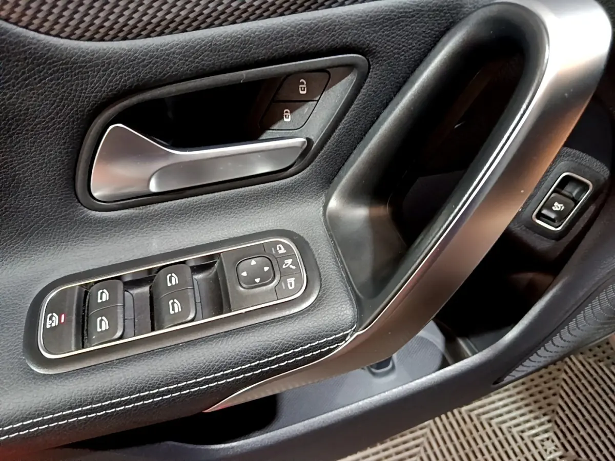Gros plan sur la poignée intérieure et les commandes de vitres côté gauche d'une Mercedes CLA 180 d Business Line gris clair.