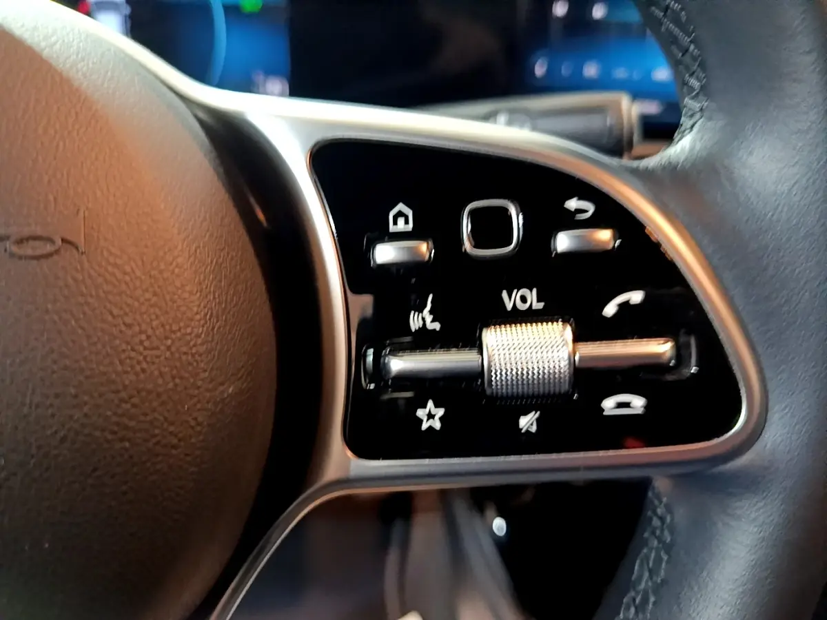 Gros plan sur les commandes multifonctions en aluminium et cuir du volant côté gauche d'une Mercedes CLA 180 d gris clair.