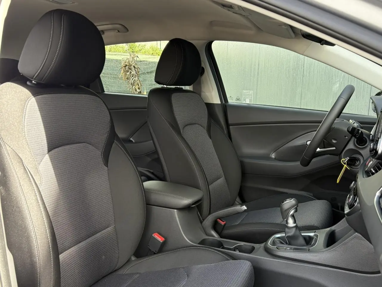 Vue intérieure côté droit montrant les sièges avant noirs et gris, accoudoir coulissant et levier de vitesses cuir de la Hyundai i30 SW 2025.