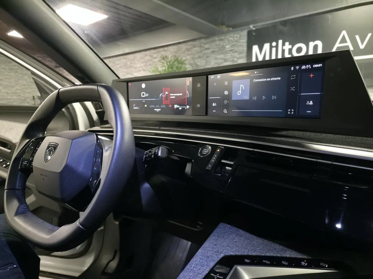 Vue intérieure côté conducteur du Peugeot 5008 blanc 2025, avec volant compact et double écran panoramique HD flottant.