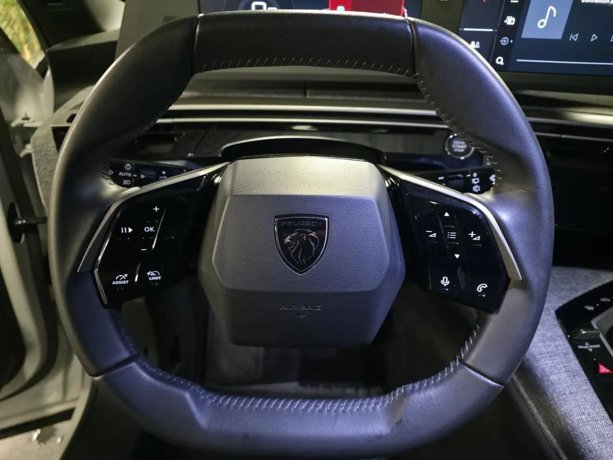 Gros plan sur le volant noir du Peugeot 5008 2025 avec logo lion et commandes intégrées, intérieur moderne.
