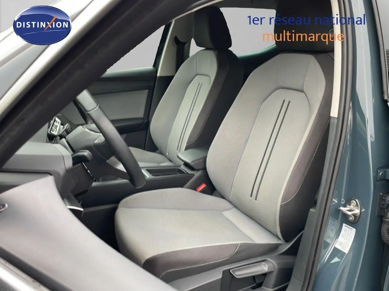 Vue intérieure côté conducteur de la SEAT LEON gris magnétique métal, montrant les sièges avant en tissu clair et tableau de bord.