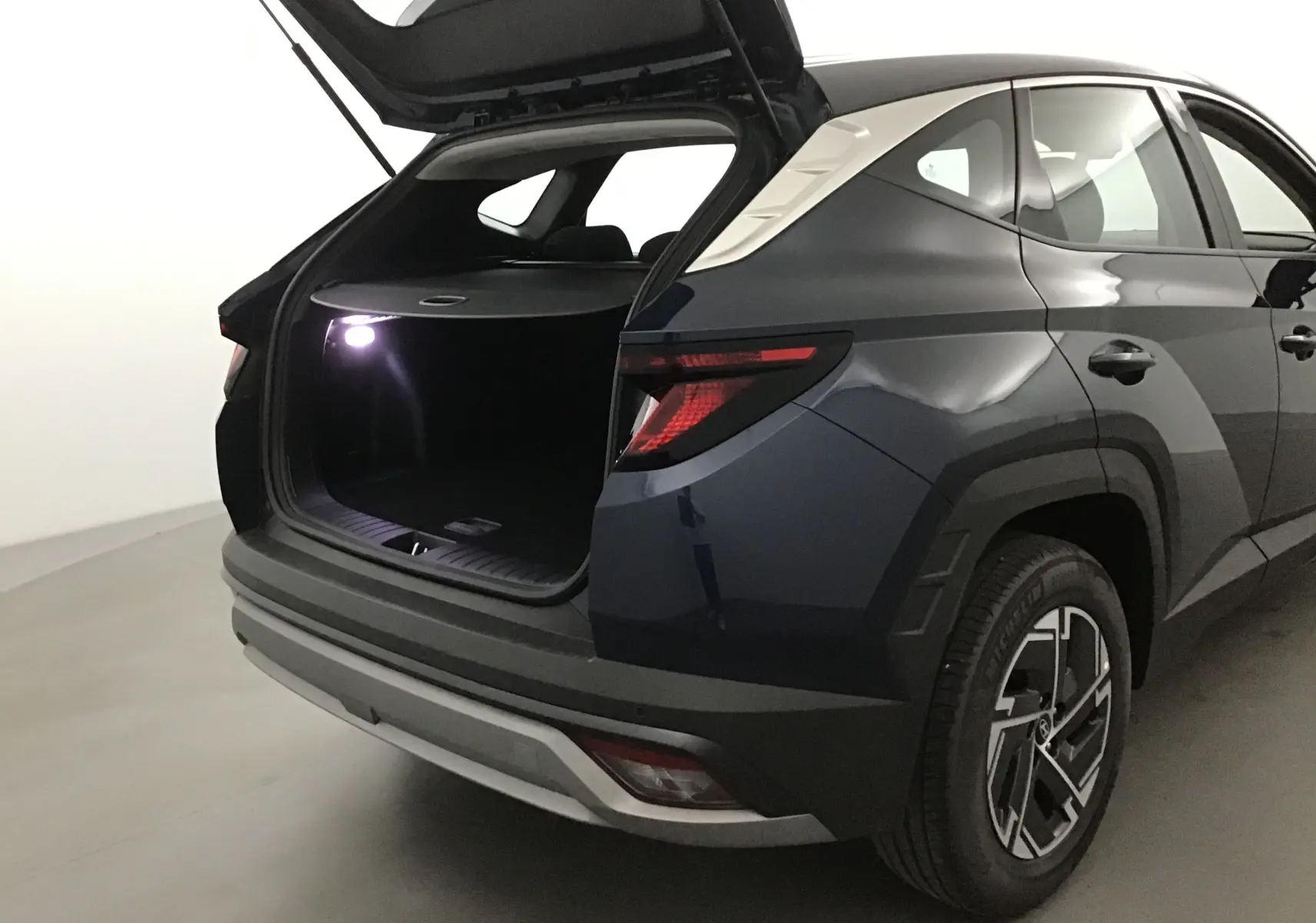 Vue arrière droite d'un Hyundai Tucson 2025 bleu Salling avec coffre ouvert et éclairage intérieur actif
