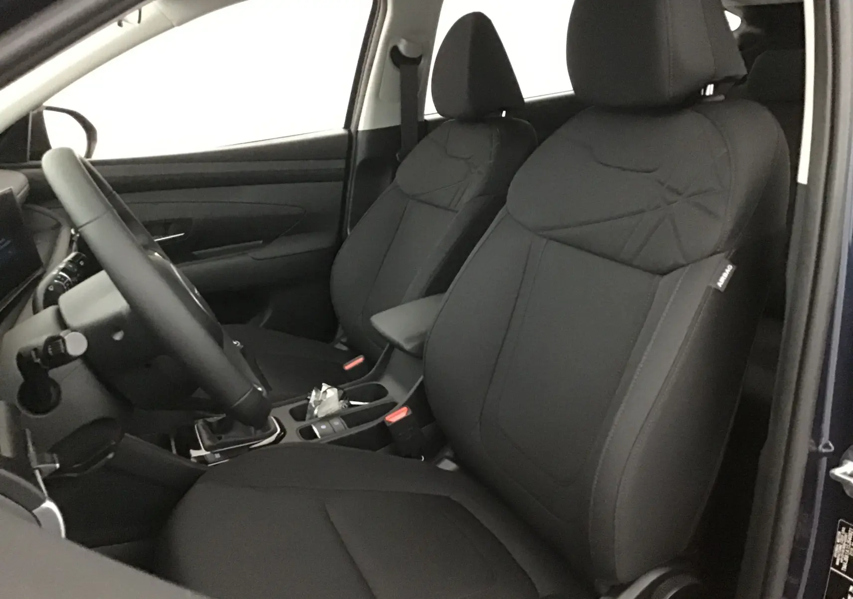 Vue intérieure côté conducteur du Hyundai Tucson 2025 bleu Salling, sièges avant en tissu noir avec volant cuir.