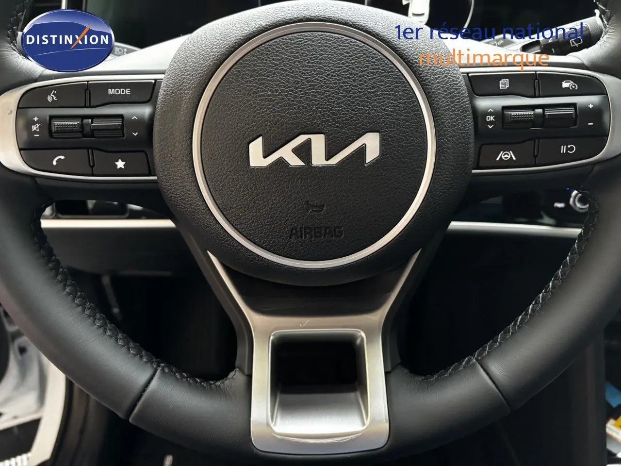 Gros plan sur le volant cuir noir du Kia Sportage 2025, mettant en valeur les commandes intégrées et le logo central.