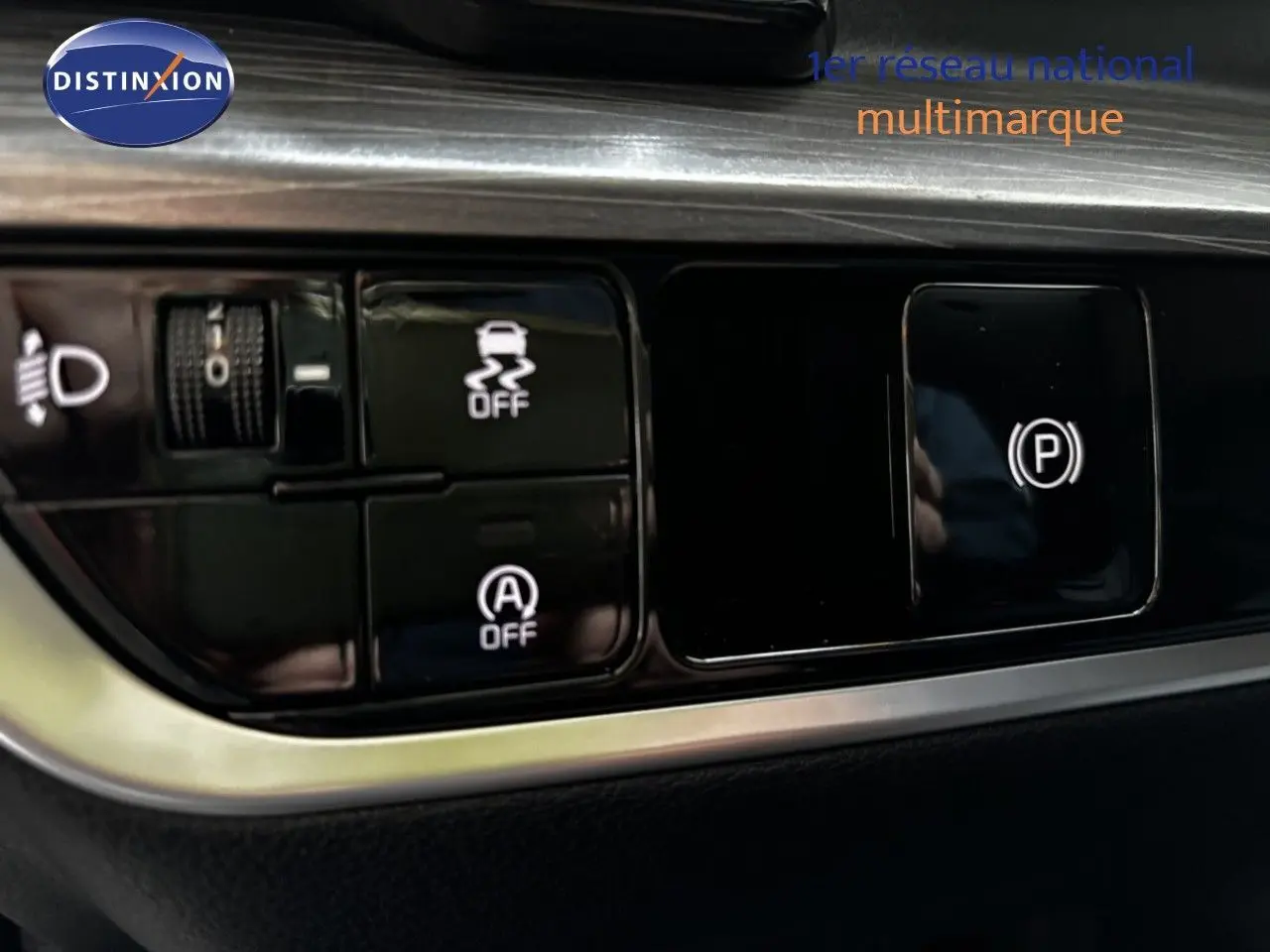 Gros plan sur les commandes noires du tableau de bord du Kia Sportage blanc nacré, avec boutons de stabilité et frein à main électronique.