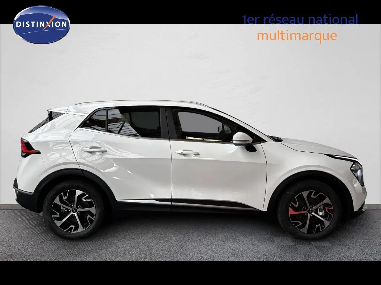 Profil latéral droit d’un KIA SPORTAGE blanc nacré métal 2025 avec jantes alliage noires et détails rouges.