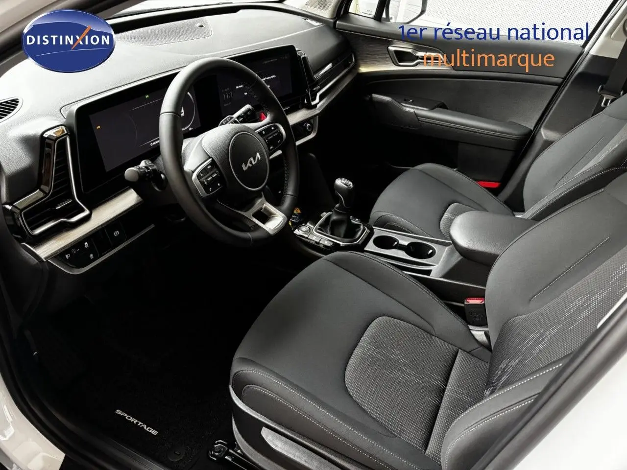 Vue intérieure avant du Kia Sportage 2025 blanc nacré, sièges noirs et tableau de bord moderne avec boîte manuelle.