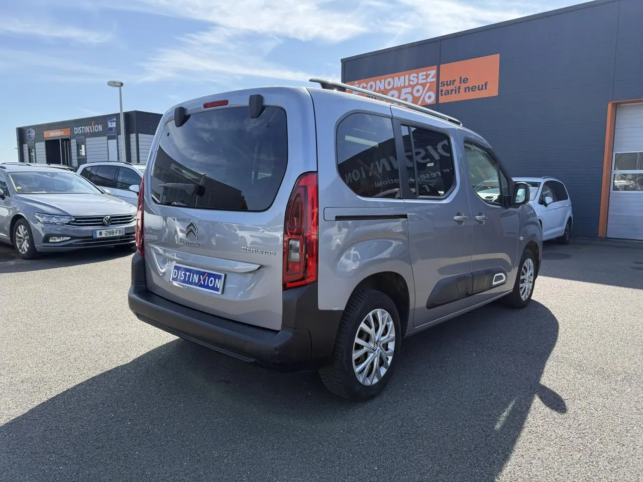 Vue 3/4 arrière droite d'un Citroën Berlingo gris foncé avec vitres arrière surteintées sur parking.