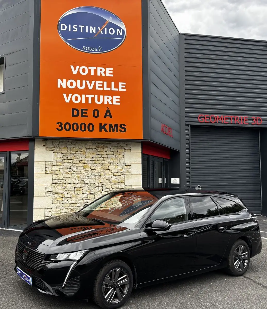 Peugeot 308 PureTech 130 noire vue en 3/4 avant droit devant un bâtiment avec panneau orange Distinxion.