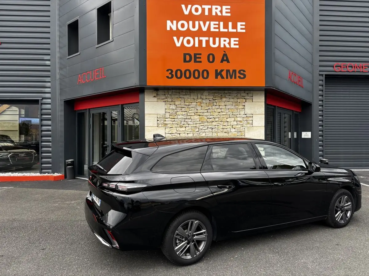 Peugeot 308 PureTech 130 noire vue de trois quarts arrière droit, stationnée devant un bâtiment moderne.