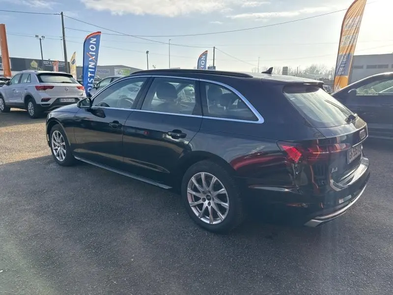 Audi A4 Avant noir brillant vue 3/4 arrière côté gauche, avec jantes alu et barres de toit noires.