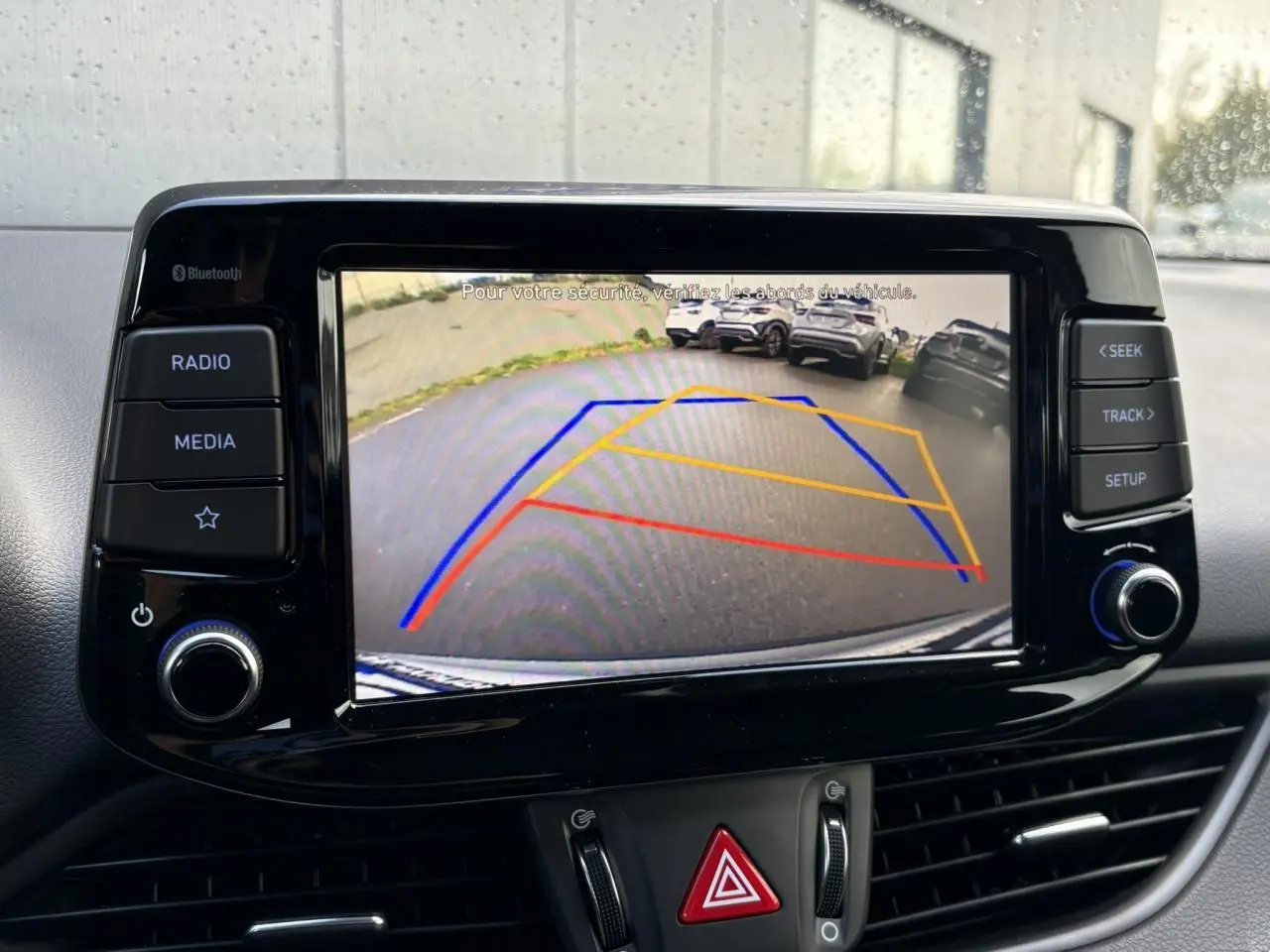Écran tactile central de la Hyundai i30 SW 2025 montrant la caméra de recul avec lignes de guidage colorées.