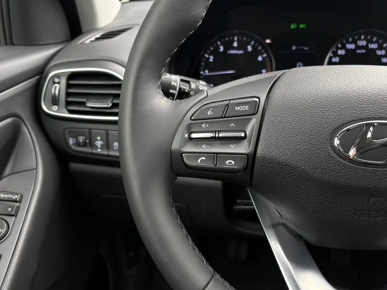 Gros plan sur le volant cuir gris foncé de la Hyundai i30 2025 avec commandes audio intégrées et tableau de bord numérique.