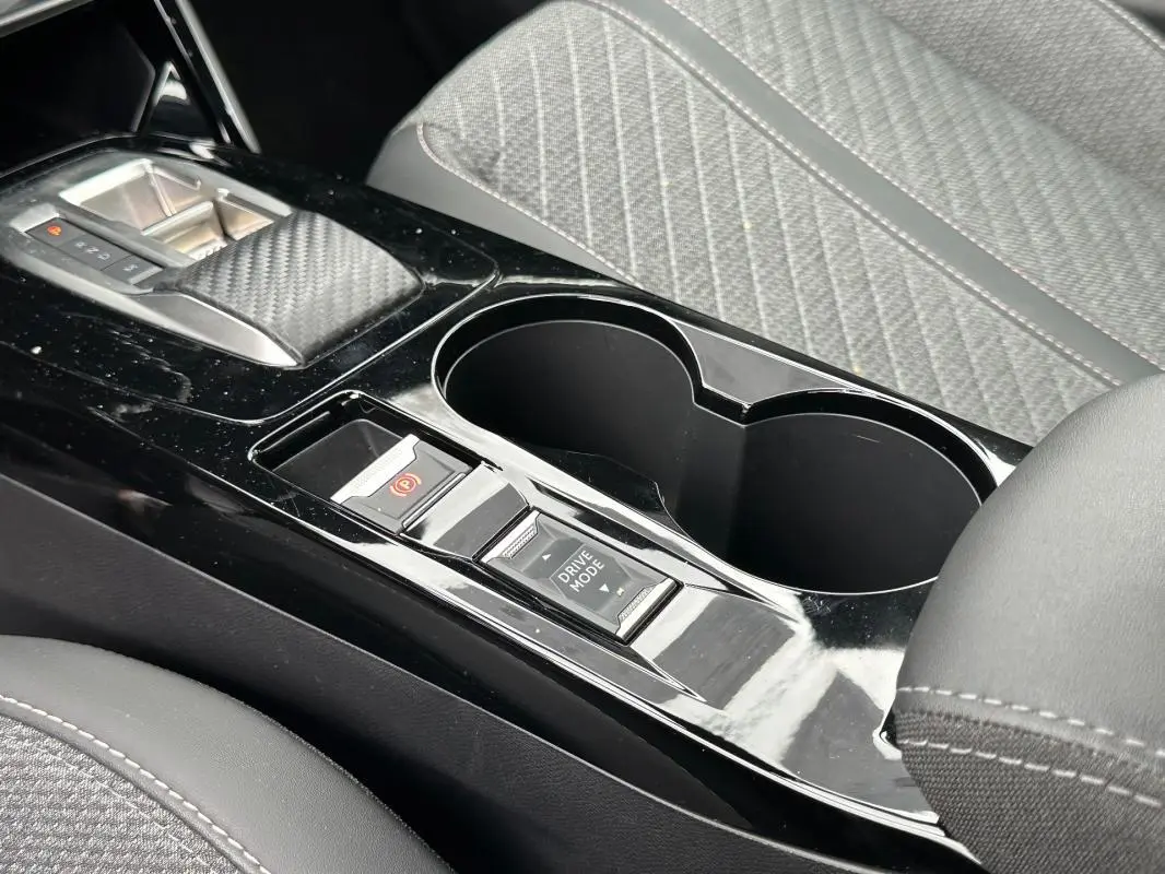 Gros plan sur la console centrale noire brillante du Peugeot 2008 Hybrid 136, avec levier de vitesse et porte-gobelets.