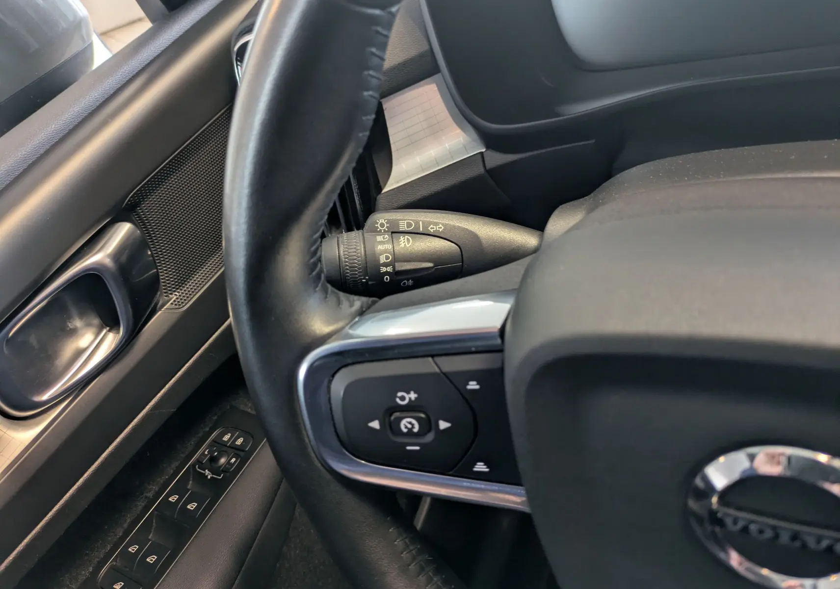 Vue rapprochée du volant côté gauche d’un Volvo XC40 marron clair, montrant les commandes au volant et la commande des phares.