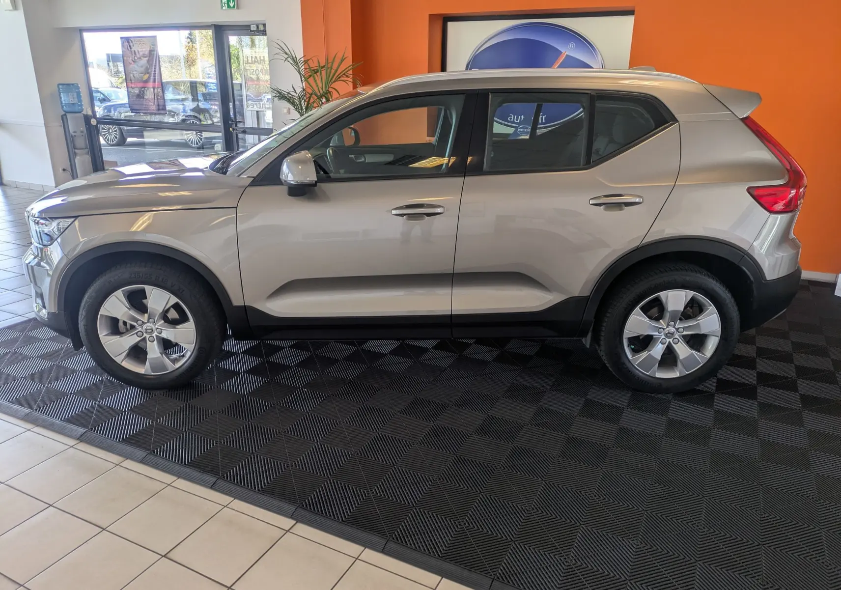 Vue de profil côté gauche d'un Volvo XC40 marron clair 2021 Momentum 2WD en showroom avec jantes alliage.