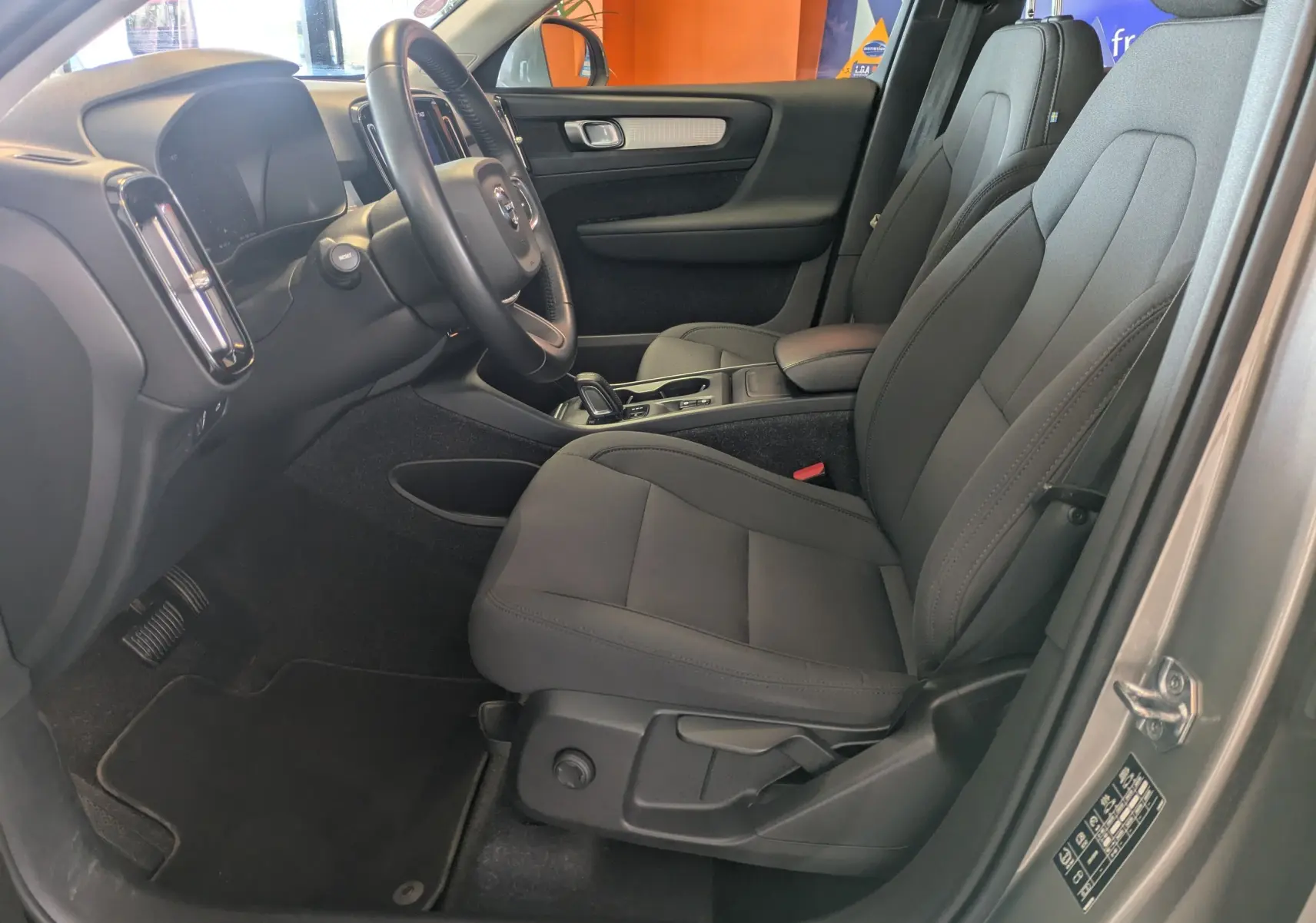 Vue intérieure côté conducteur du Volvo XC40 Momentum 2021, sièges gris et tableau de bord noir avec volant cuir.