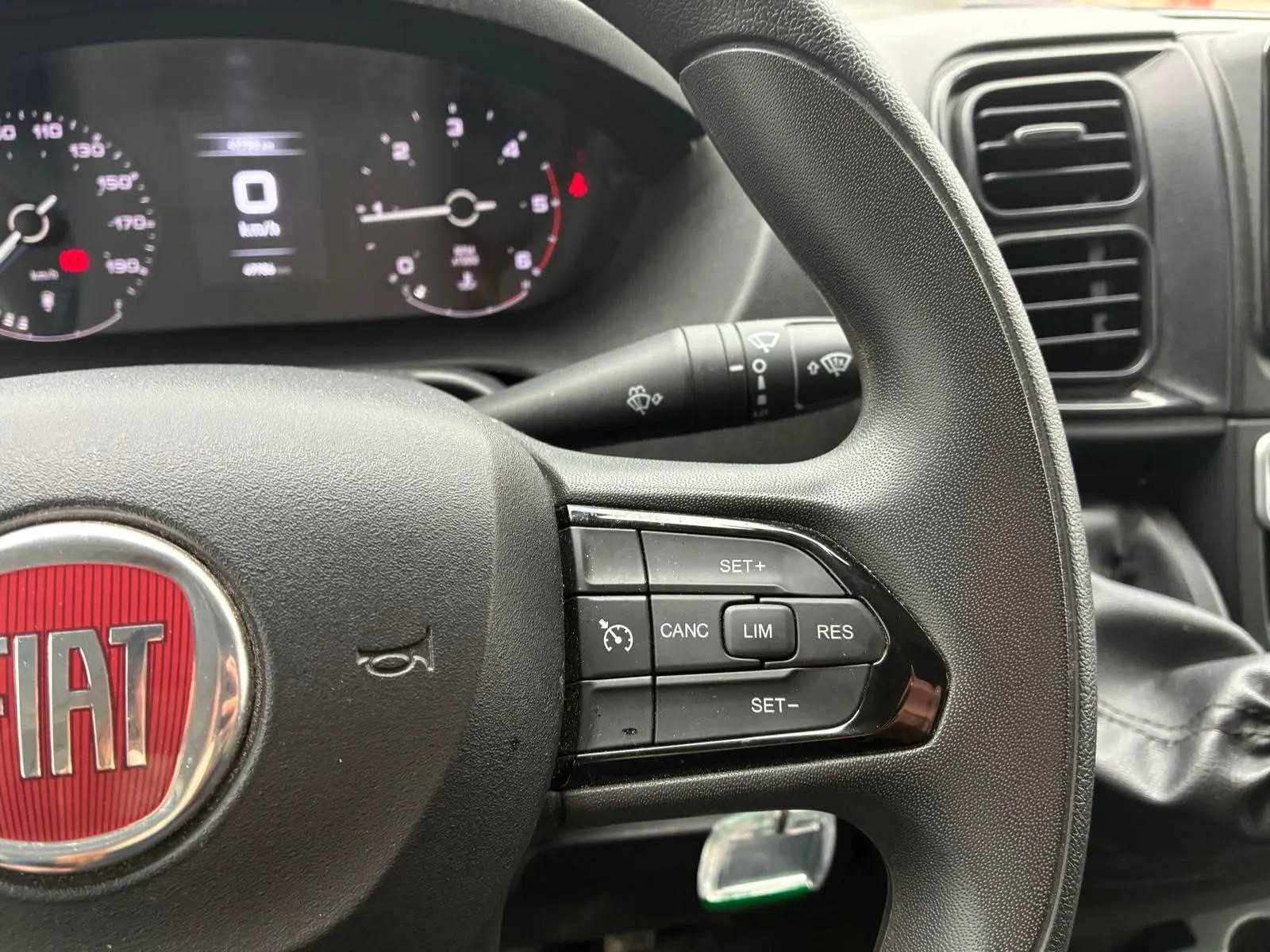 Gros plan sur le volant noir du Fiat Ducato Fourgon 2023 avec commandes de régulateur de vitesse et tableau de bord numérique.