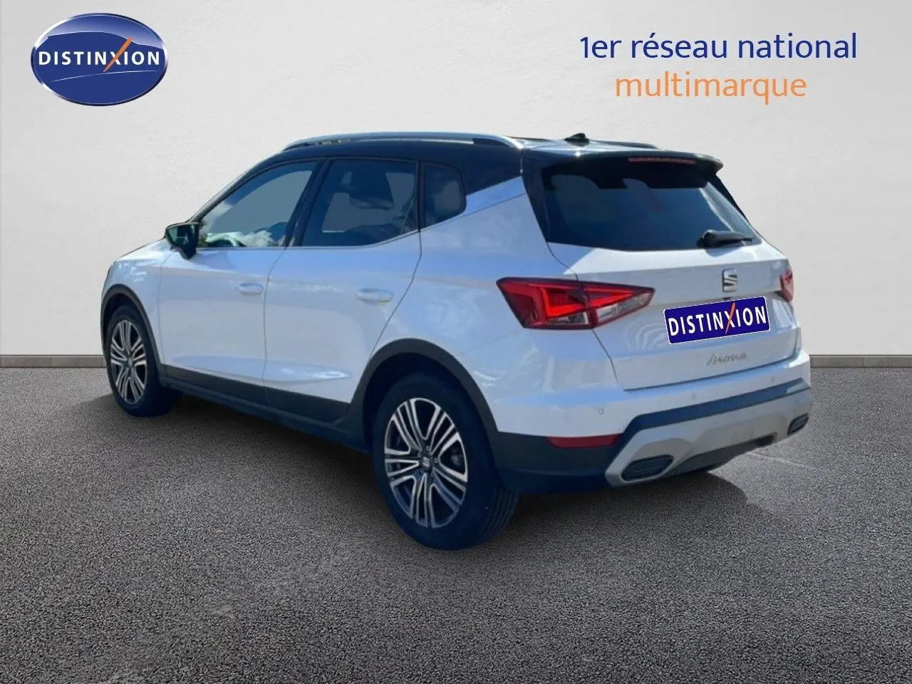 Vue 3/4 arrière droite d’un SEAT Arona blanc avec toit noir et jantes alliage, sur fond neutre intérieur showroom.