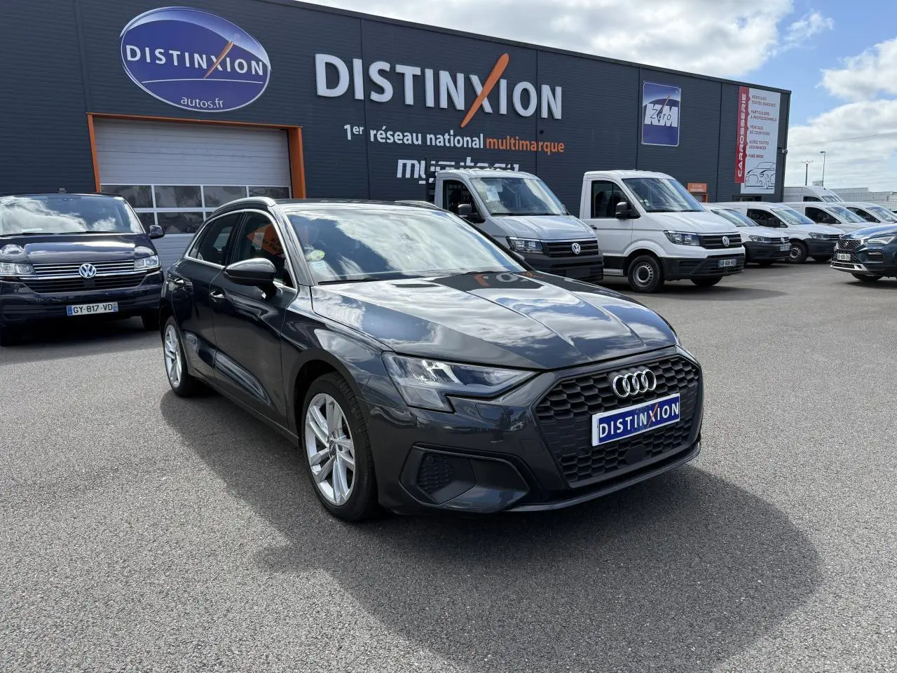 Audi A3 Sportback gris Manhattan métallisé vue 3/4 avant droit sur parking devant concession multimarque Distinxion
