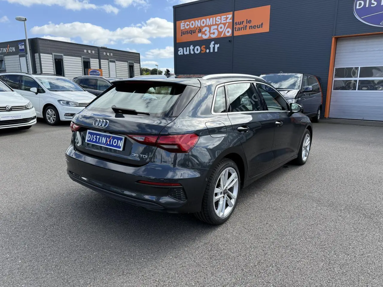 Audi A3 Sportback gris Manhattan métallisé vue 3/4 arrière droit sur parking avec jantes argentées.