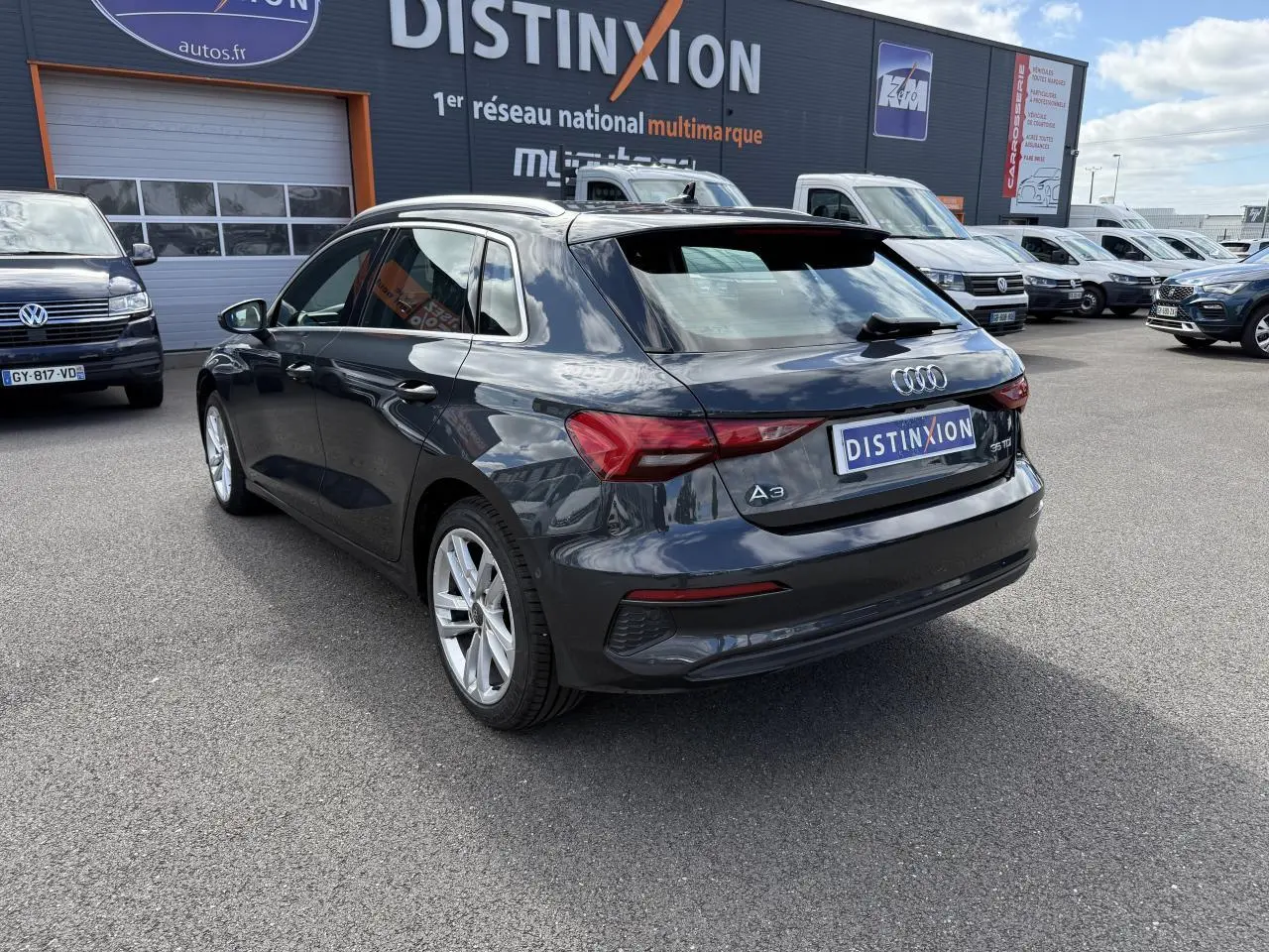 Audi A3 Sportback gris Manhattan métallisé vue 3/4 arrière droit sur parking devant concession multimarque.