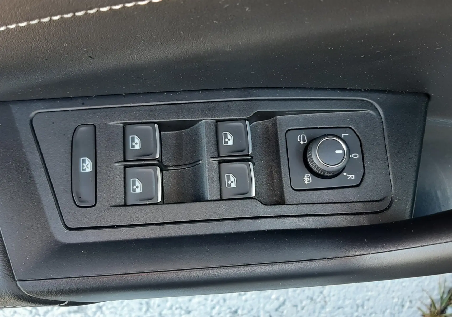 Gros plan sur les commandes de lève-vitres et réglage des rétroviseurs côté conducteur du Volkswagen T-Roc gris Indium 2024.