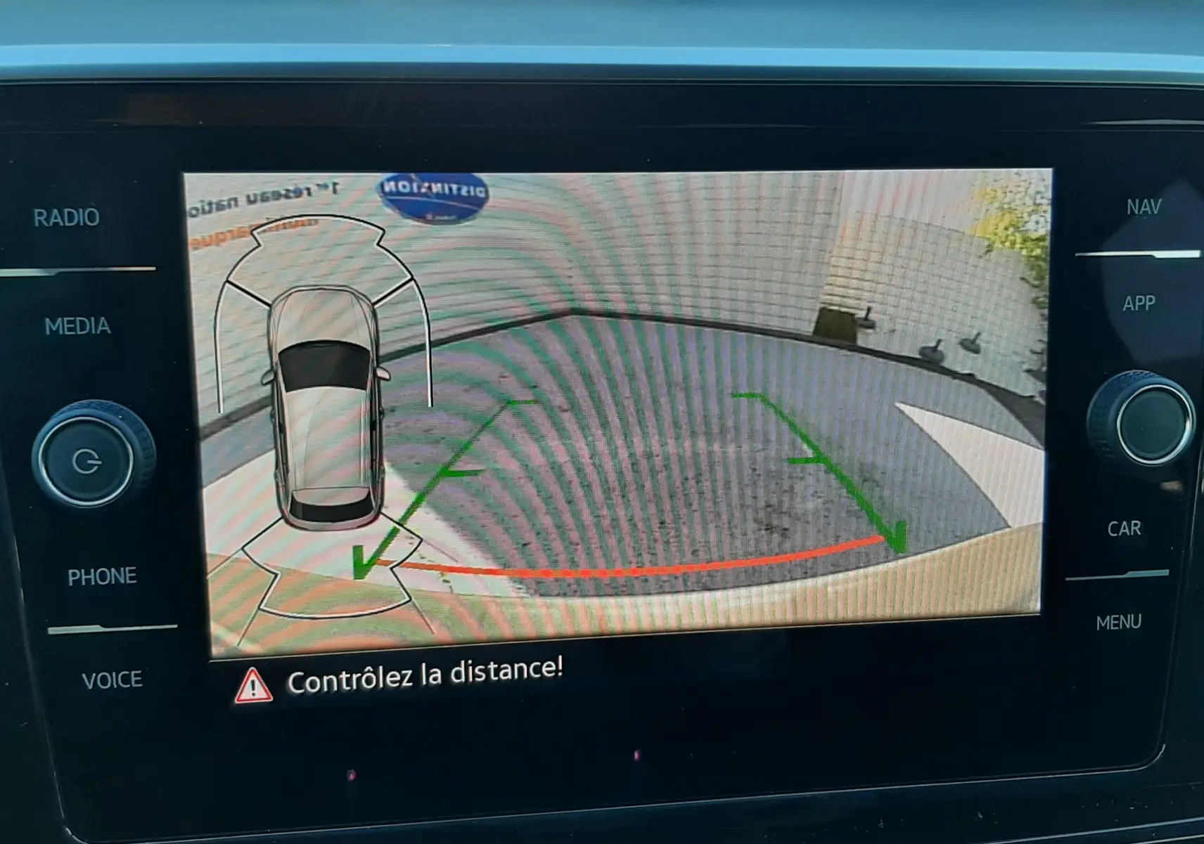 Écran de caméra de recul du Volkswagen T-Roc gris Indium, affichant les lignes de guidage et l'alerte de distance.