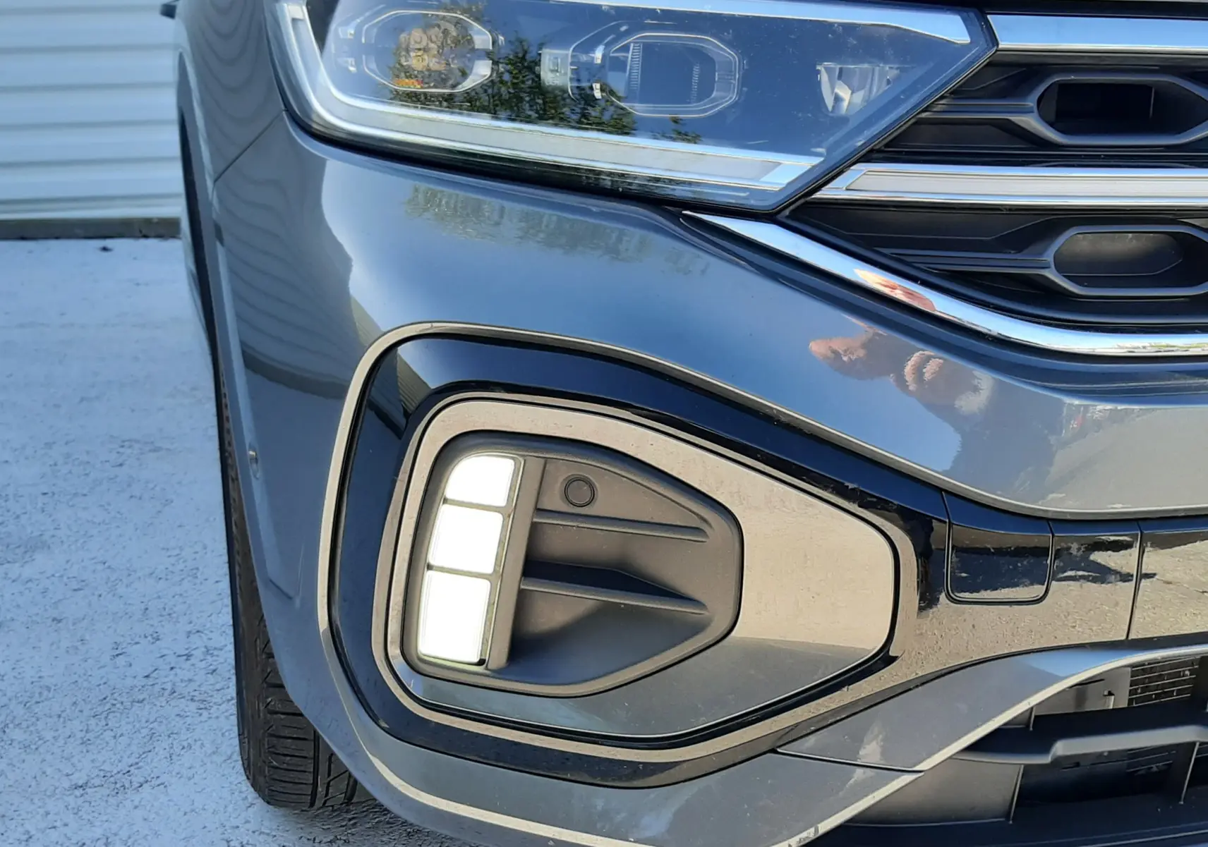 Gros plan sur l'avant gauche du Volkswagen T-Roc gris Indium, mettant en valeur le phare LED et le feu antibrouillard.