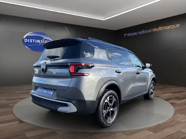 Vue 3/4 arrière droite d'un Citroën C3 Aircross hybride gris foncé avec jantes noires et toit noir dans un showroom.