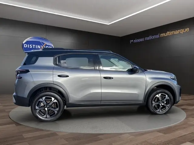 Profil droit d'un Citroën C3 Aircross hybride gris foncé avec jantes distinctives et barres de toit noires en showroom.