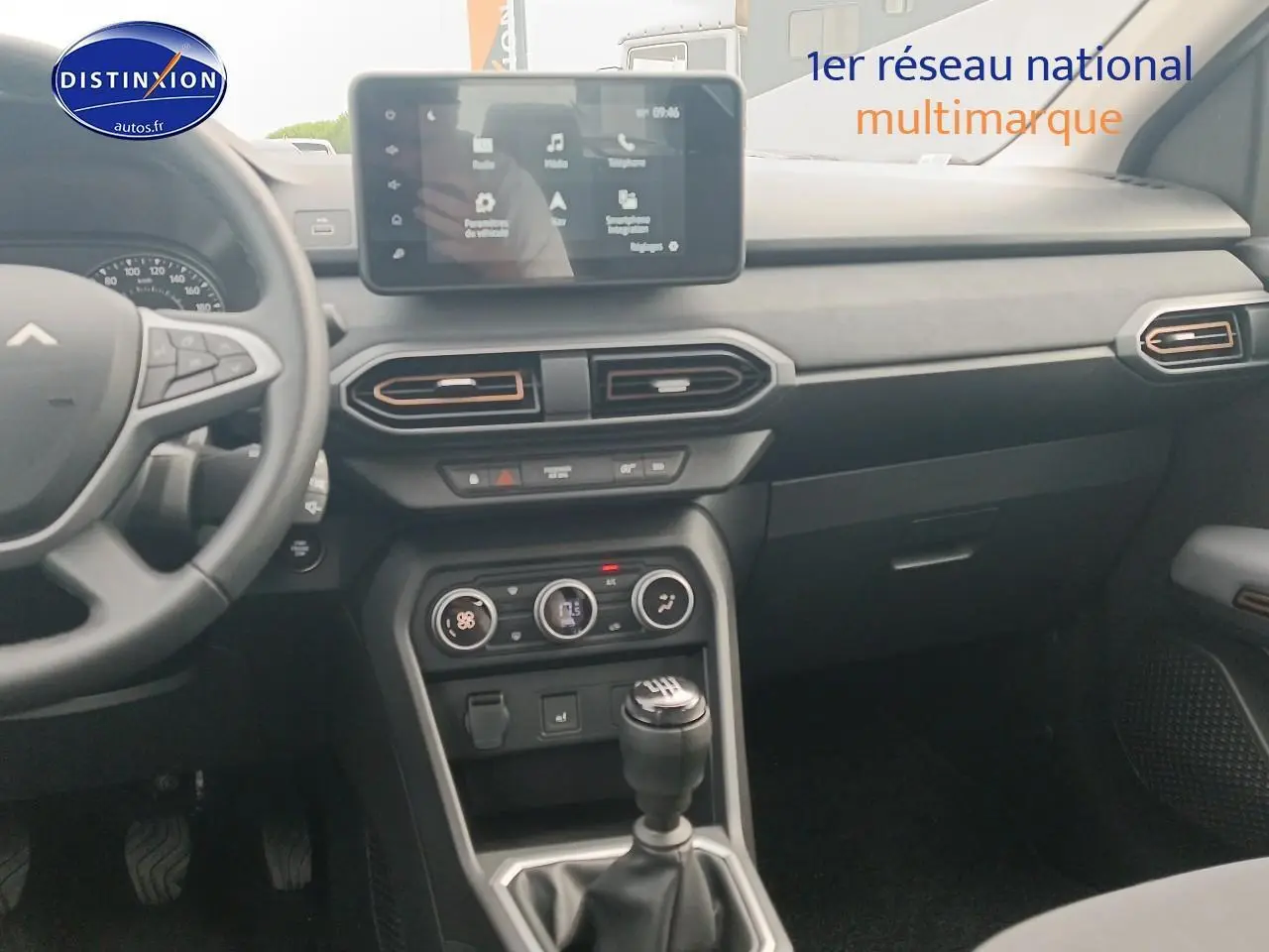 Intérieur de la Dacia Sandero 2025 vue de face, tableau de bord noir avec écran tactile et boîte manuelle.