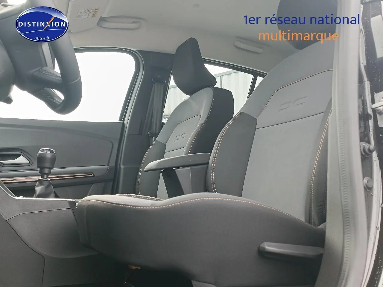 Intérieur avant de la Dacia Sandero noire 2025, vue côté conducteur avec sièges et accoudoir central visibles.