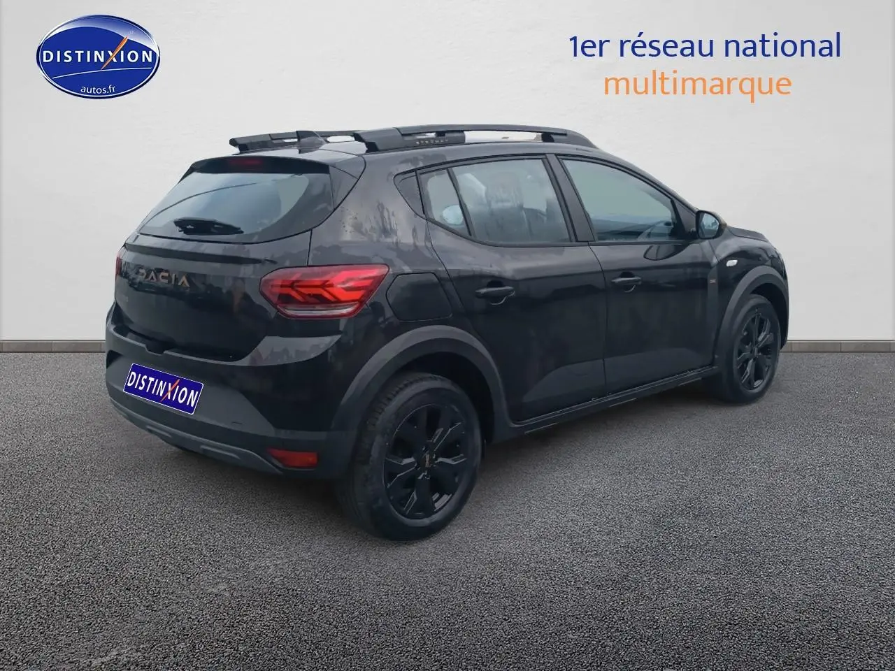 Vue 3/4 arrière droite d'une Dacia Sandero noire avec barres de toit et jantes alu noires sur fond neutre.