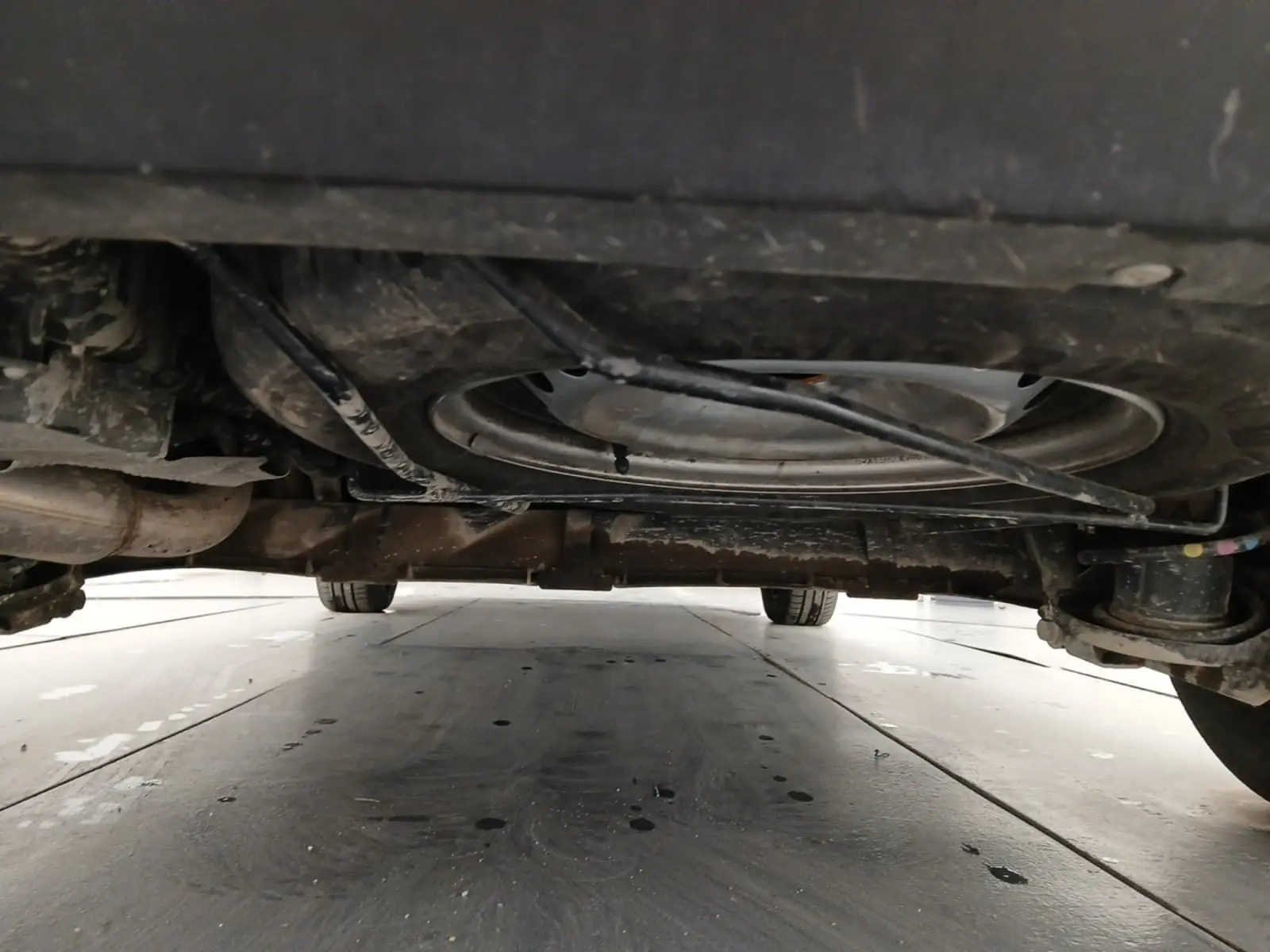 Vue en contre-plongée sous un Renault Kangoo blanc 2024, montrant la roue de secours et le châssis arrière.