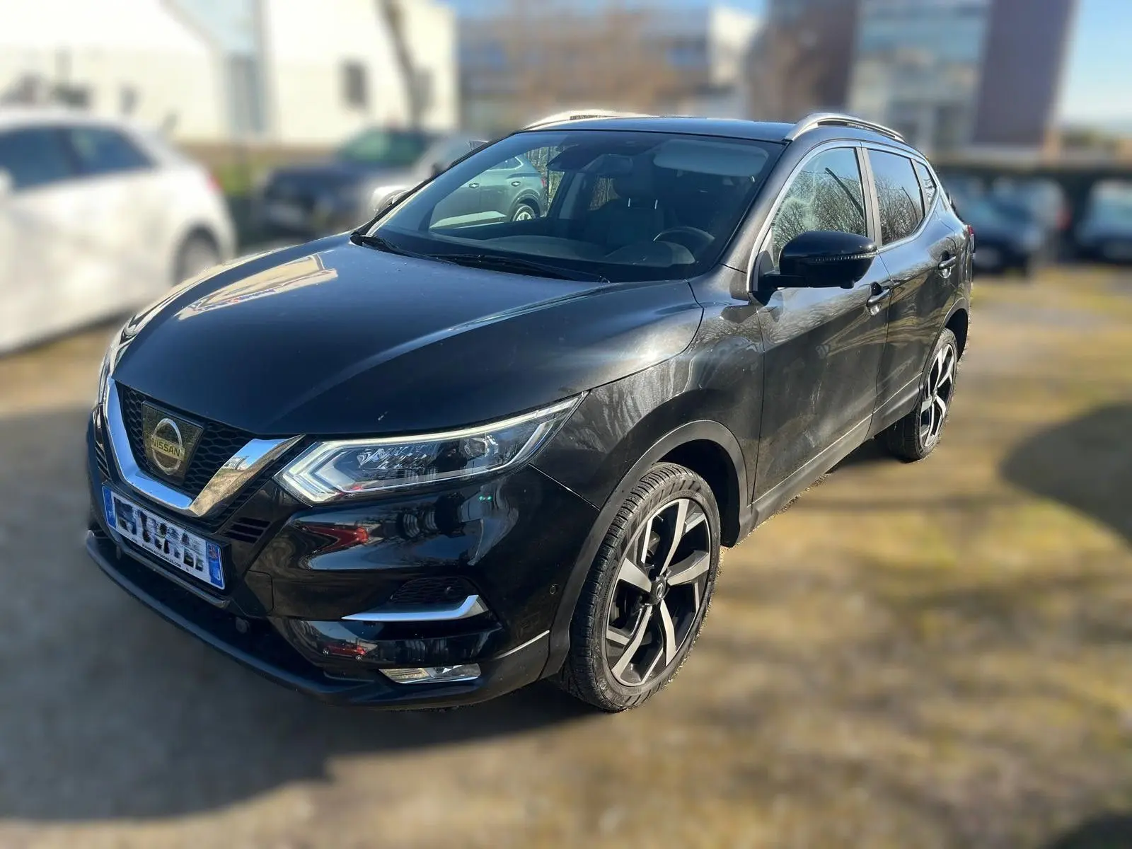 Nissan Qashqai noir vu en 3/4 avant droit, avec jantes alliage et barres de toit visibles.
