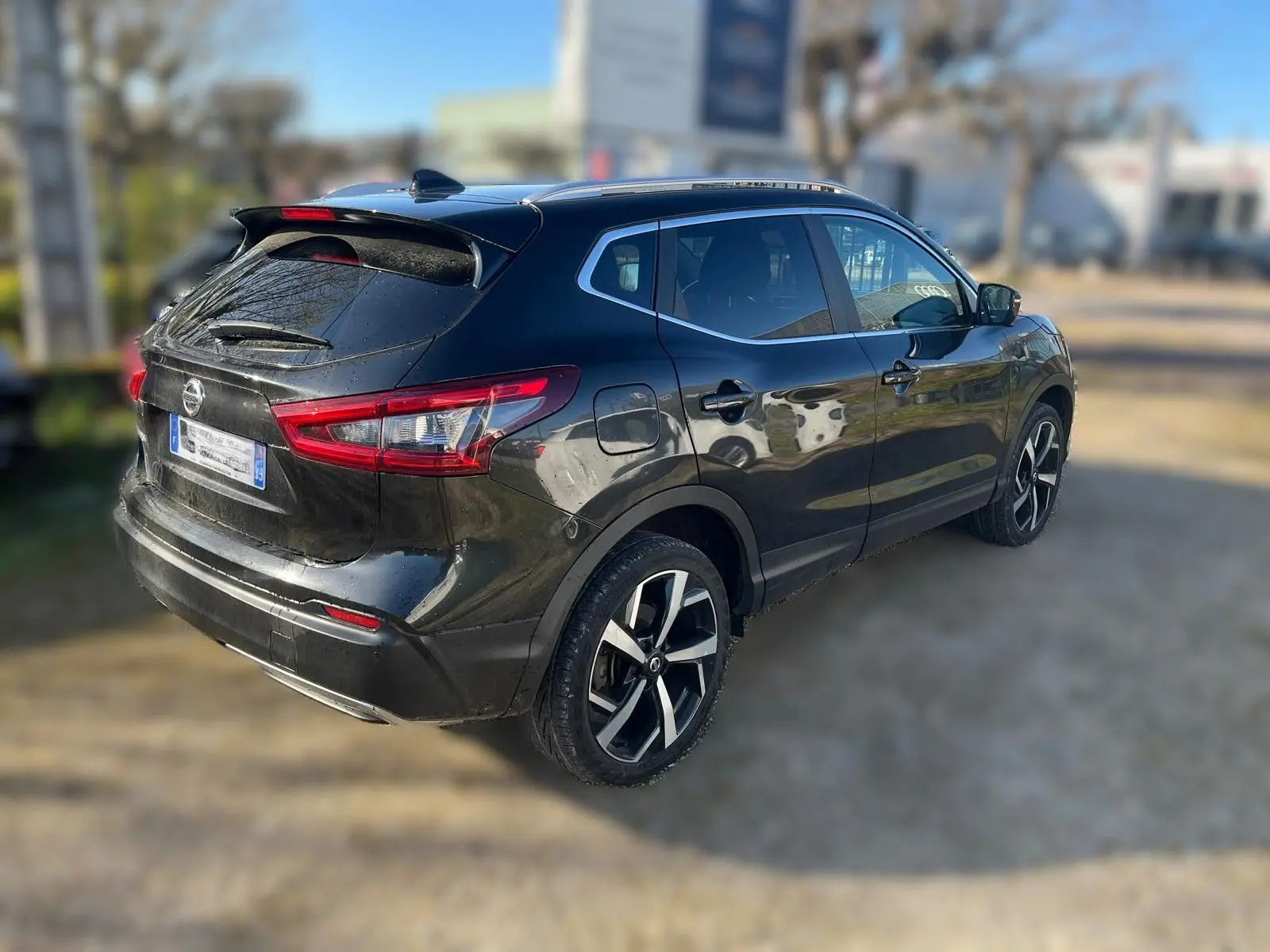 Nissan Qashqai noir en 3/4 arrière droit, avec jantes alu et toit panoramique visible au soleil.