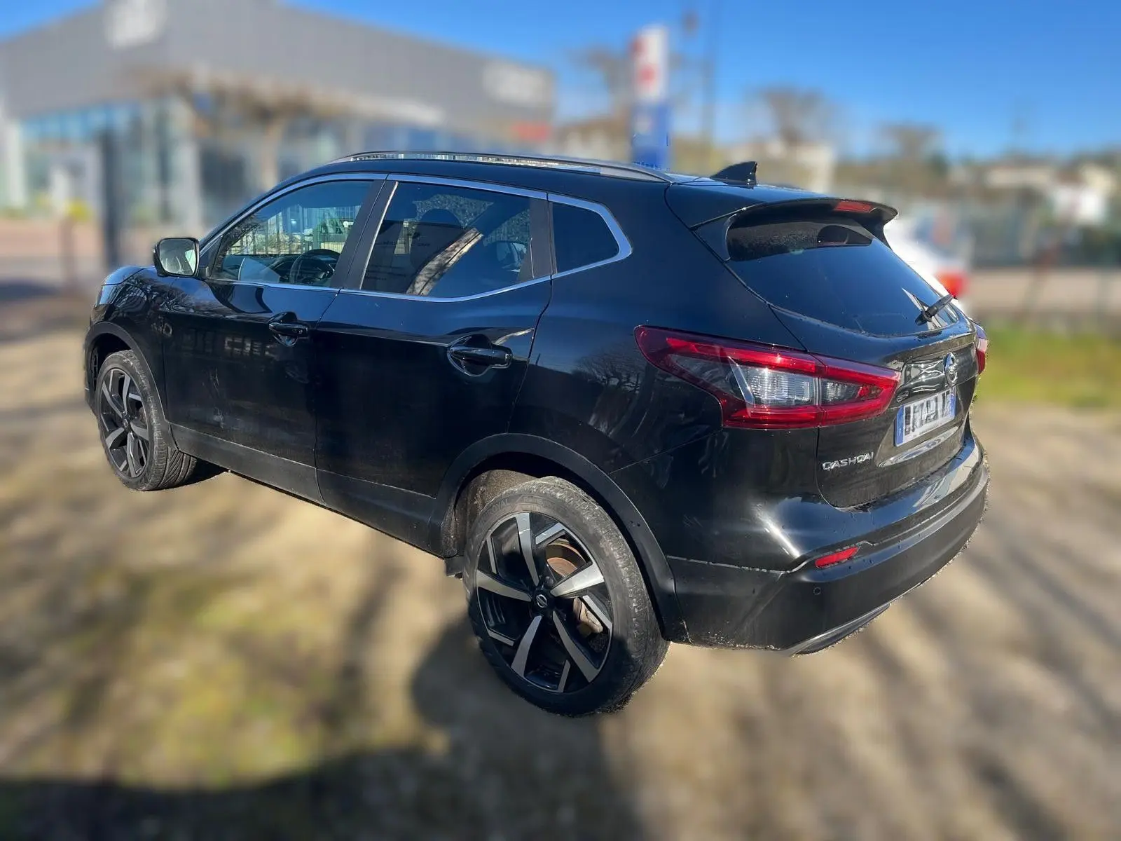 Vue 3/4 arrière droite d'un Nissan Qashqai noir avec jantes alliage et barres de toit visibles.