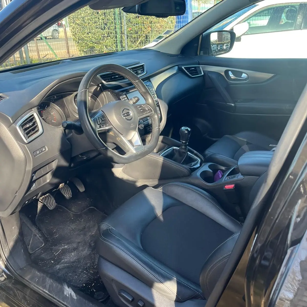 Vue intérieure côté conducteur du Nissan Qashqai noir avec volant cuir multifonctions et boîte manuelle.