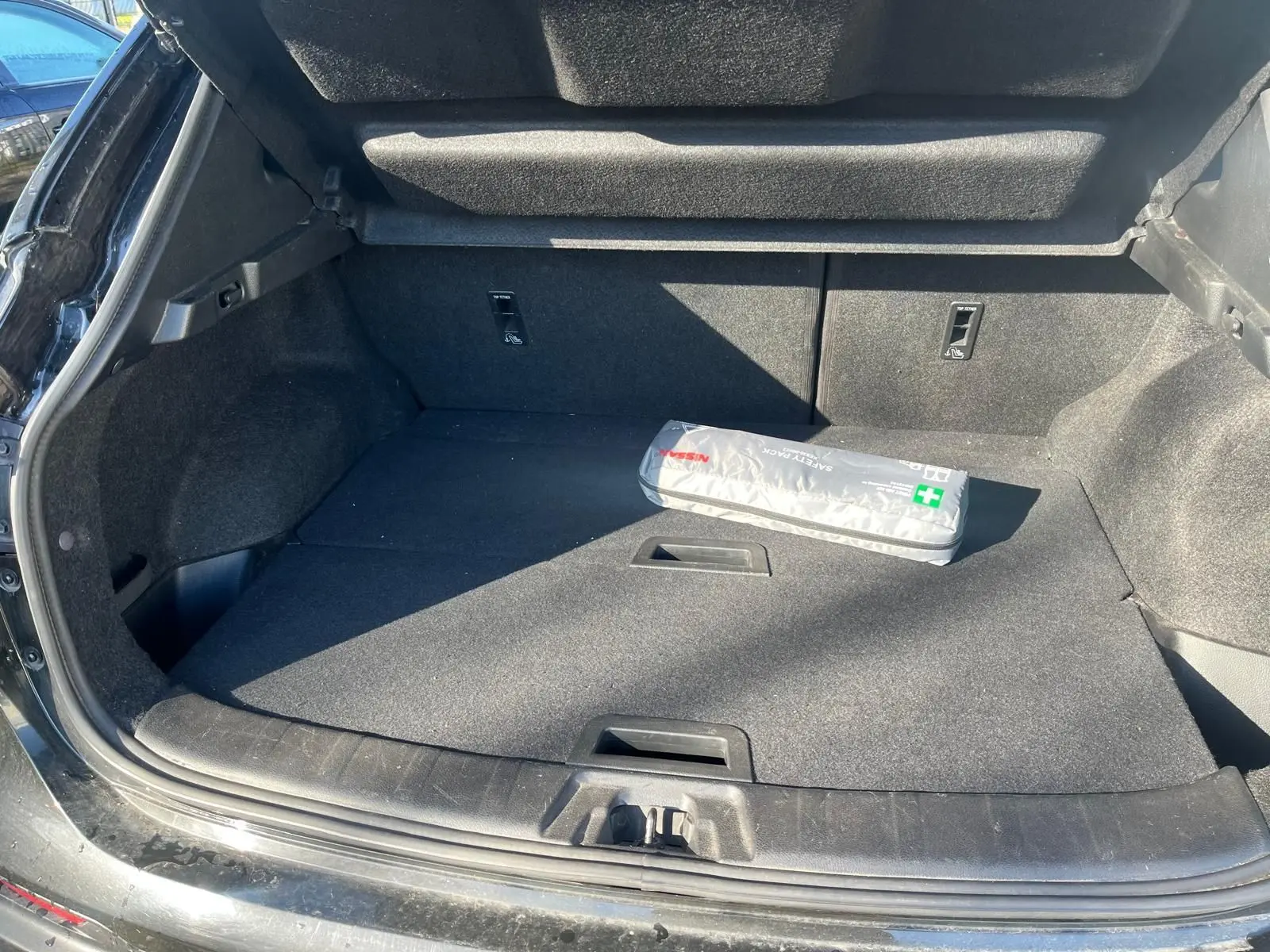 Coffre ouvert vu de l'arrière d'un Nissan Qashqai noir avec trousse de secours Nissan posée à l'intérieur.