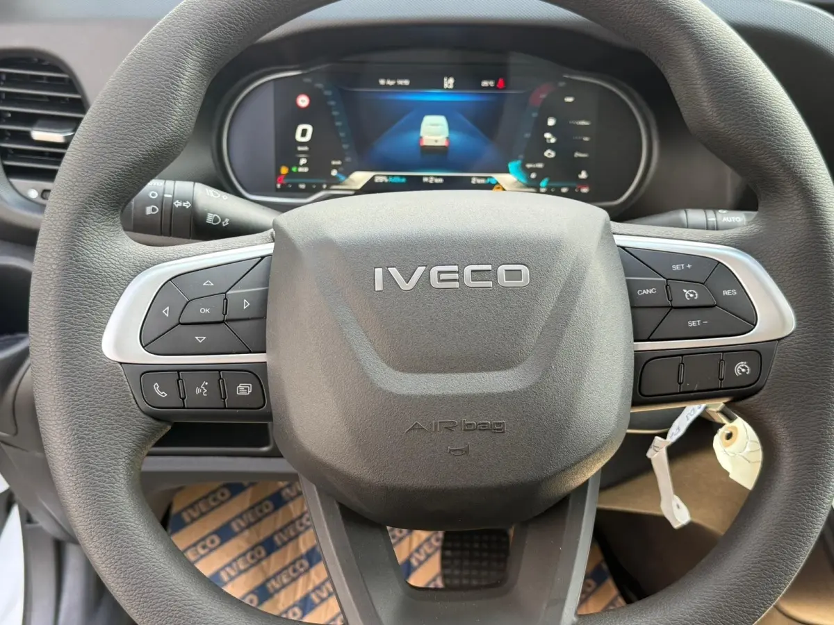 Vue rapprochée du volant noir Iveco avec commandes intégrées et tableau de bord numérique en arrière-plan.