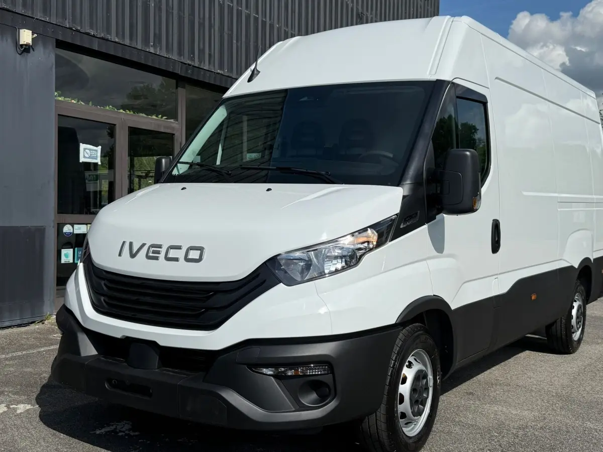 Vue 3/4 avant d’un utilitaire Iveco Daily blanc avec calandre noire et pare-chocs noir, stationné devant un bâtiment.