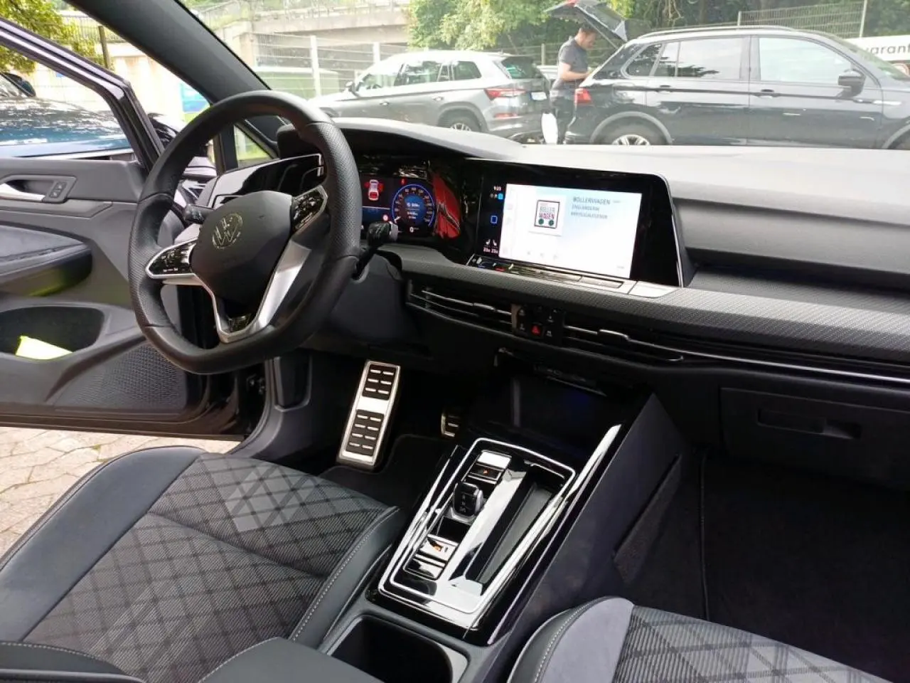 Intérieur de Volkswagen Golf 1.5 eTSI 2024, vue côté conducteur, volant cuir, écran tactile et sièges sport noirs à motifs.