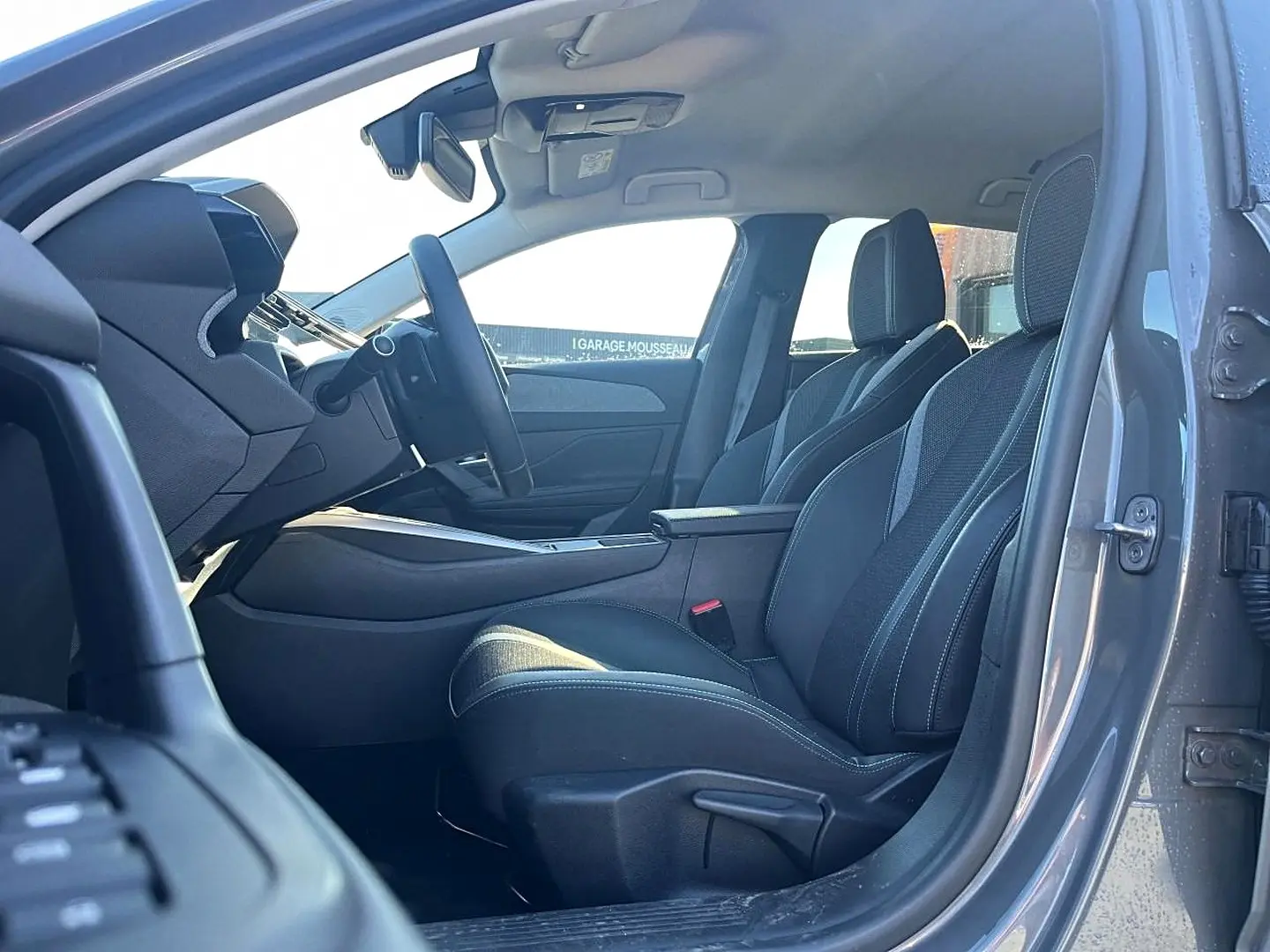 Intérieur avant droit d’une Peugeot 308 gris selenium, sièges tissu noir avec surpiqûres claires et accoudoir central.