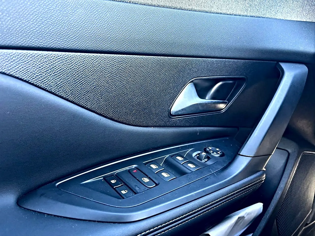Détail de la porte côté gauche noire avec commandes électriques des vitres et poignée intérieure du Peugeot 308 gris selenium.