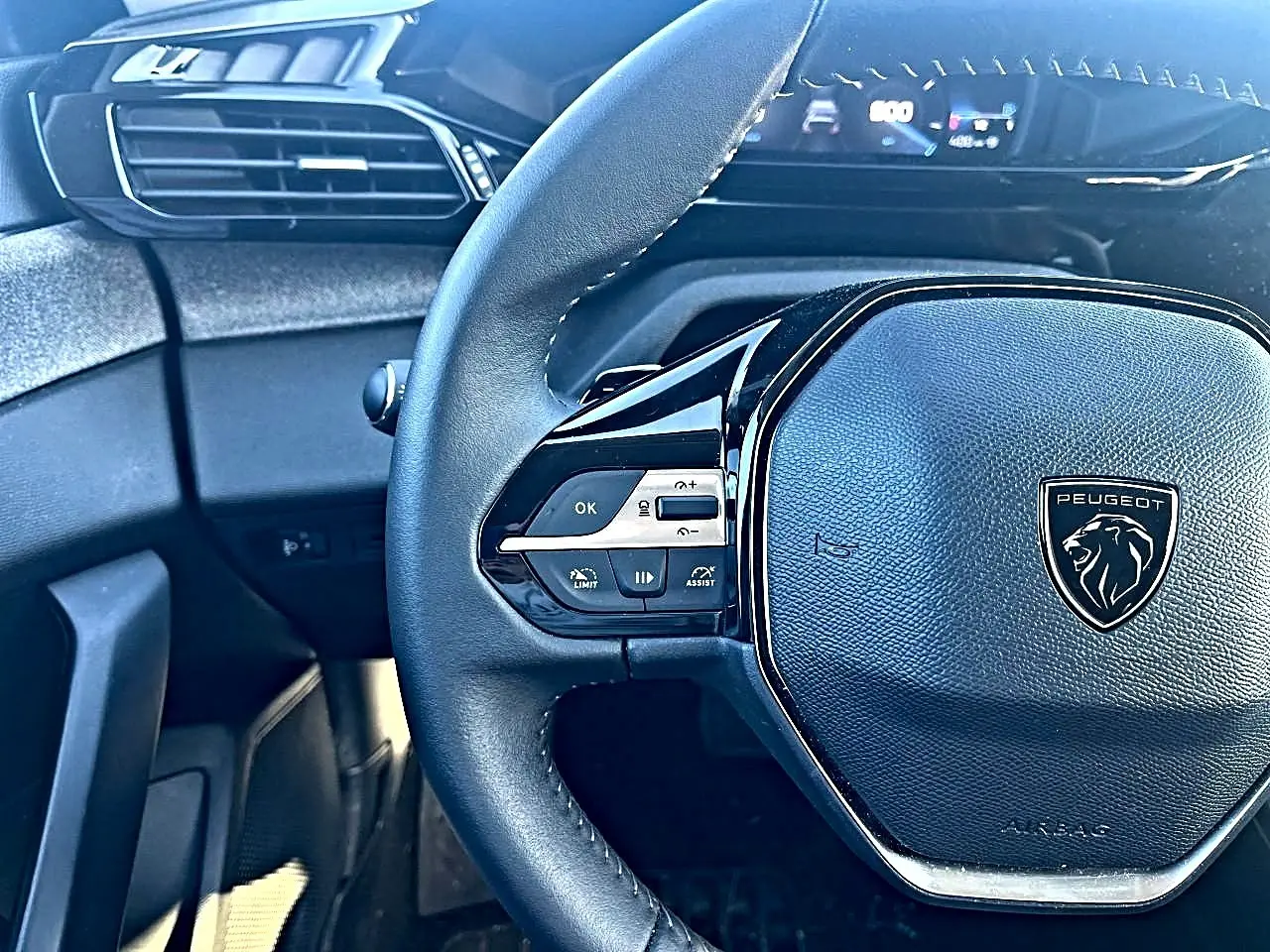 Vue rapprochée du volant multifonction noir de la Peugeot 308 2025 avec tableau de bord numérique en arrière-plan.