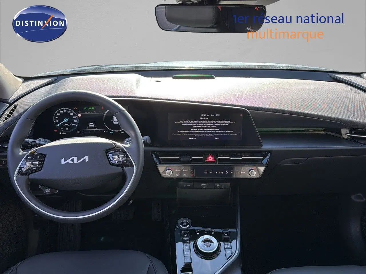 Intérieur moderne du Kia Niro 2025 en vue frontale, tableau de bord noir avec écran tactile et volant multifonction.
