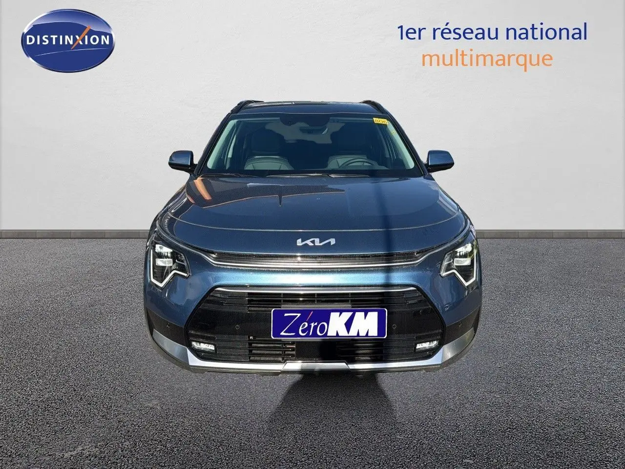 Vue frontale d'un KIA NIRO bleu minéral métal 2025 avec calandre noire et phares LED distinctifs allumés.